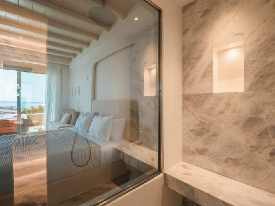 Deluxe Suite with Outdoor Hot Tub: Luxury bedroom with a sea view through a glass wall and marble bathroom details