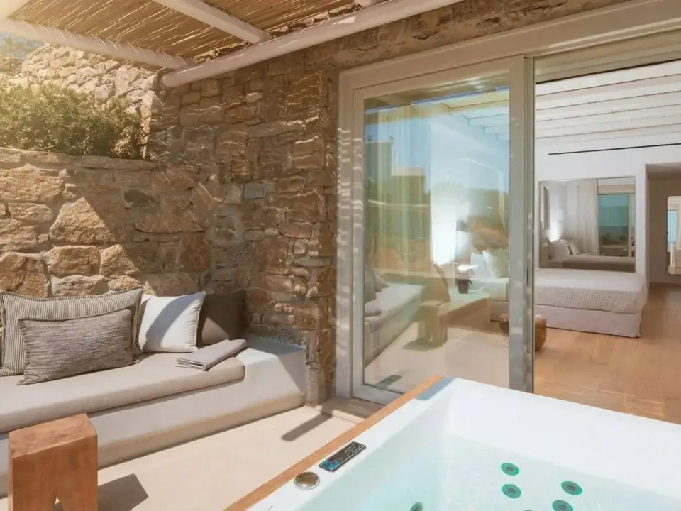 Deluxe Suite with Outdoor Hot Tub: Luxury outdoor patio with a built-in bench beside a stone wall and a hot tub looking into a bedroom suite