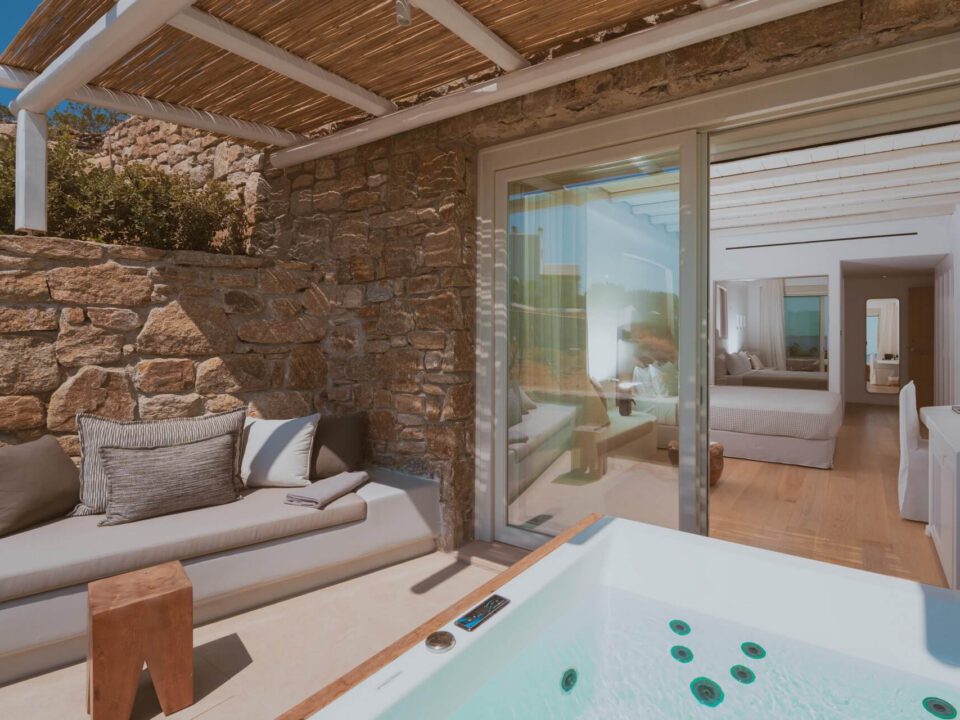 Deluxe Suite with Outdoor Hot Tub: Luxury patio with a hot tub, stone bench seating, and a view into a modern bedroom