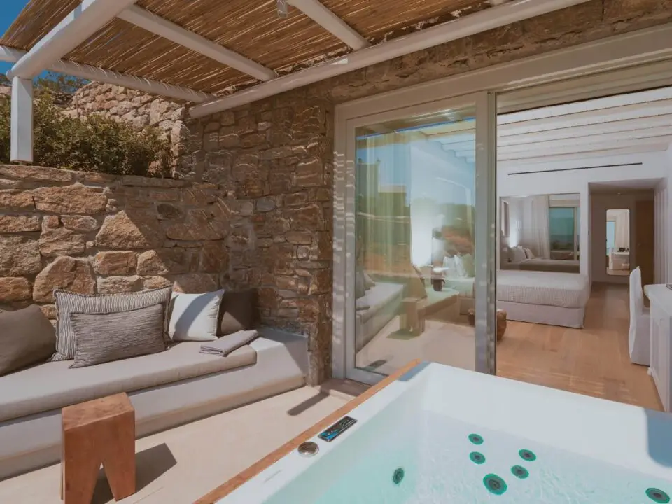 Deluxe Suite with Outdoor Hot Tub: Luxury patio with a hot tub, stone bench seating, and a view into a modern bedroom