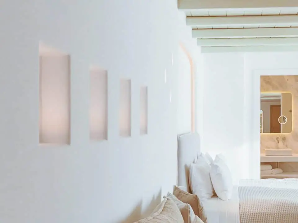 Exclusive Suite with Outdoor Hot Tub: Bright minimalist bedroom with white bedding, pillows, and a built-in bathroom vanity visible in the background