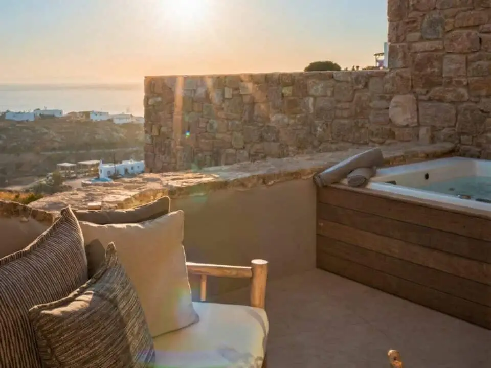 Exclusive Suite with Outdoor Hot Tub: Sunset view from a stone terrace with a sofa, hot tub, and champagne setup overlooking the sea