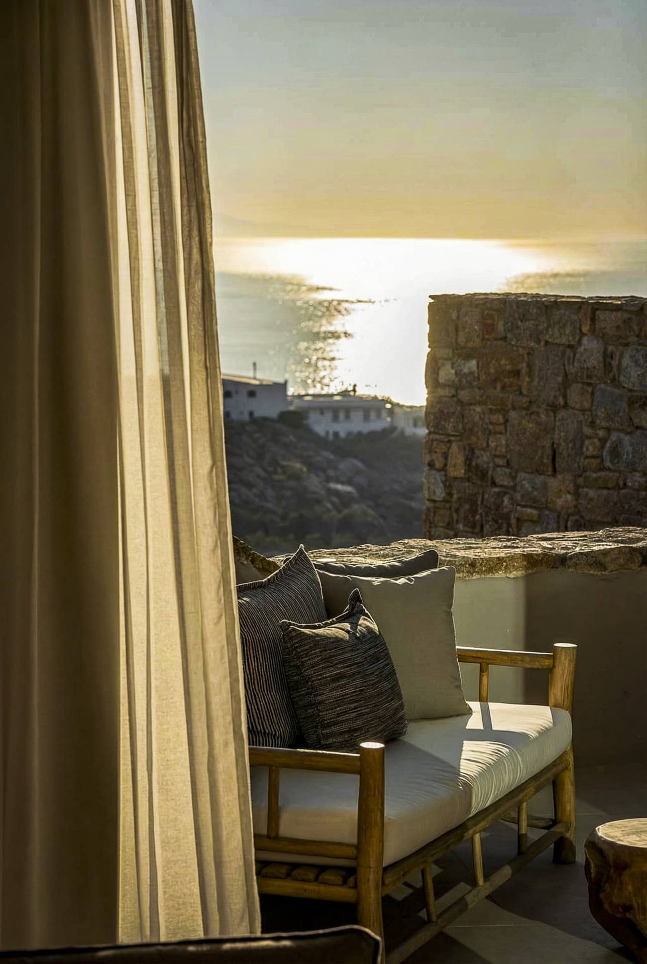 Exclusive Suite with Outdoor Hot Tub: A cushioned chair on a balcony overlooks the sunlit sea at sunset