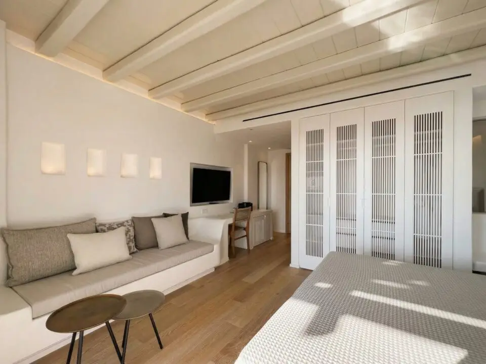 Junior Suite with Outdoor Hot Tub: Modern minimalist bedroom with a built-in sofa, wall-mounted TV, and white slatted closet doors