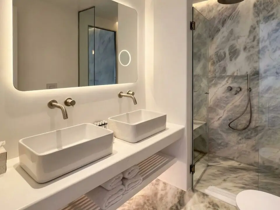 Junior Suite with Outdoor Hot Tub: Modern bathroom with double sinks, backlit mirror, and glass shower with marble walls and floor