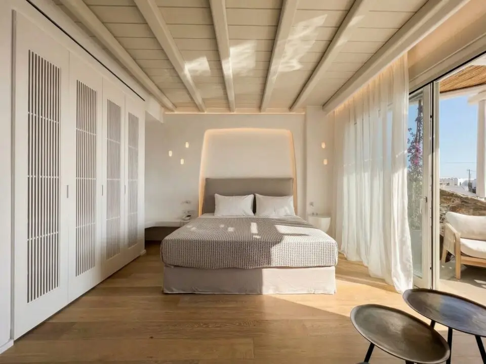 Junior Suite with Outdoor Hot Tub: Bright minimalist bedroom with a king-sized bed, white built-in closets, and sunlight through sheer curtains and a glass door