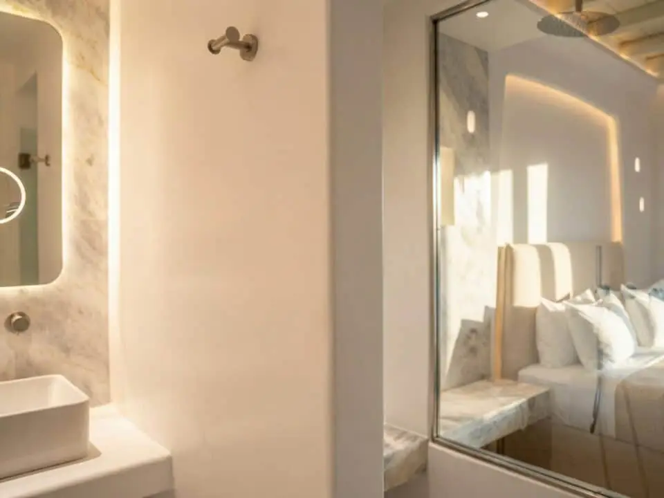 Junior Suite with Outdoor Hot Tub: Luxury bathroom with illuminated mirror and sink with a glass window overlooking the bedroom with a bed and pillows