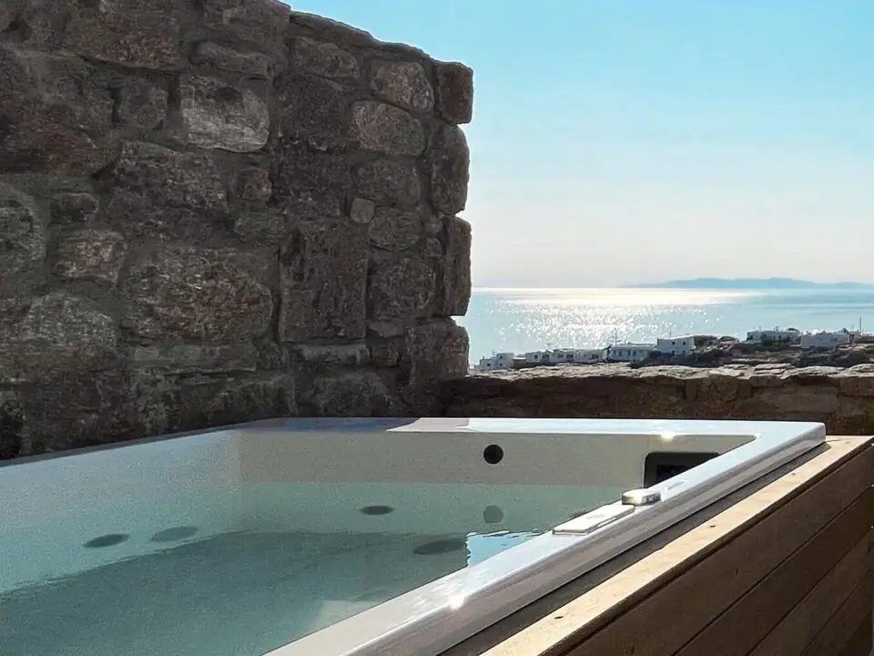 Junior Suite with Outdoor Hot Tub: Outdoor hot tub with a sea view beside a stone wall under a bright sun
