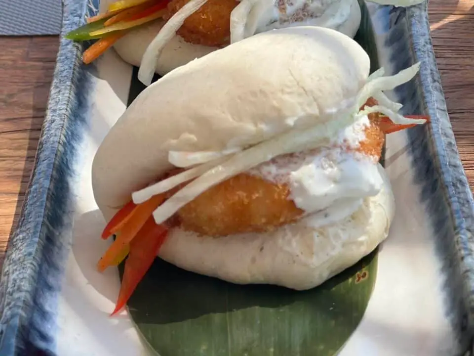 Nomia Mykonos Sunset Suites Menu: Two steamed bao buns filled with fried shrimps, slaw, and creamy sauce on a plate