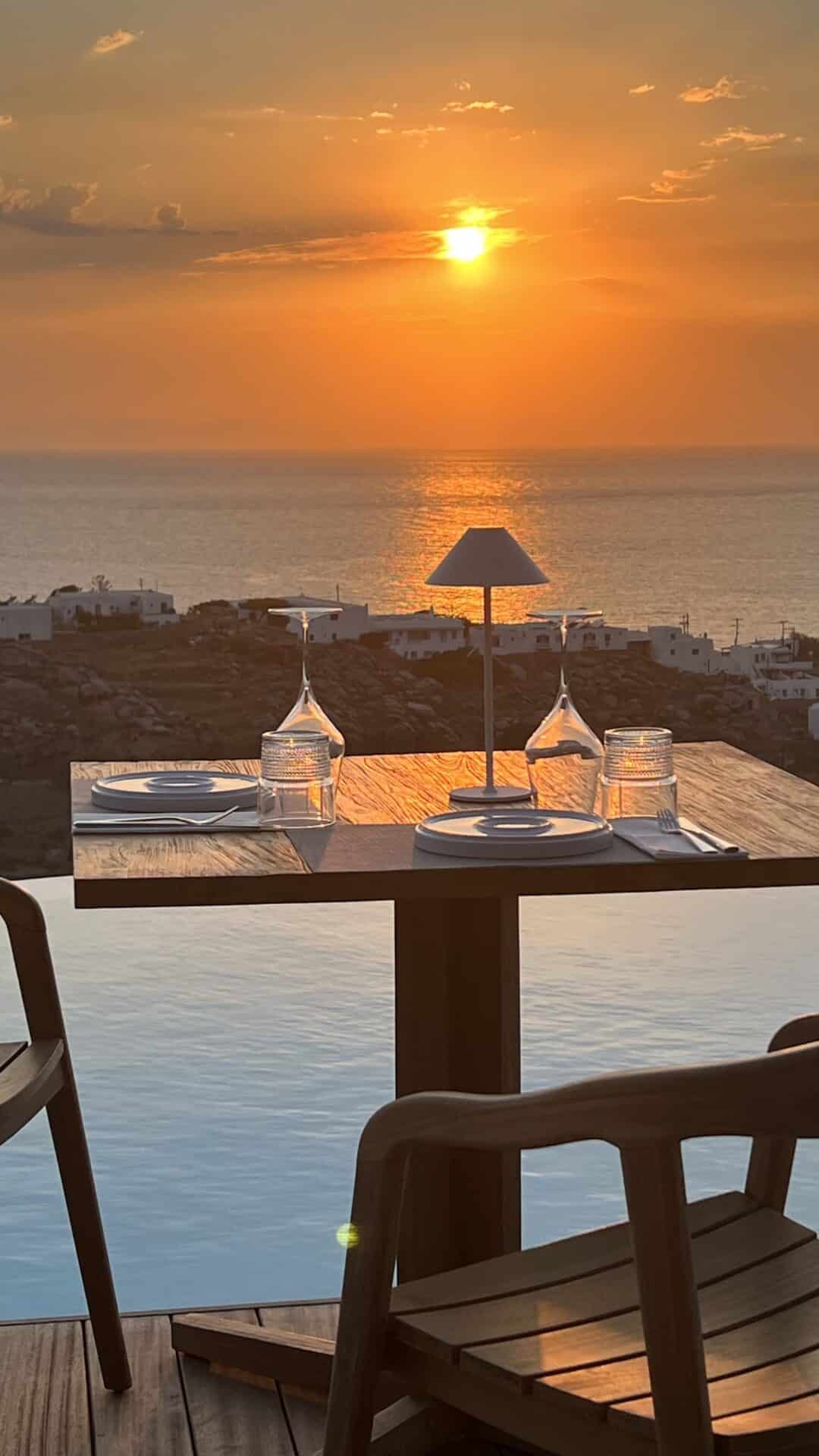 Nomia Mykonos Sunset Suites Restaurant: Sunset over the Aegean viewed from Nomia's seaside restaurant table set for two