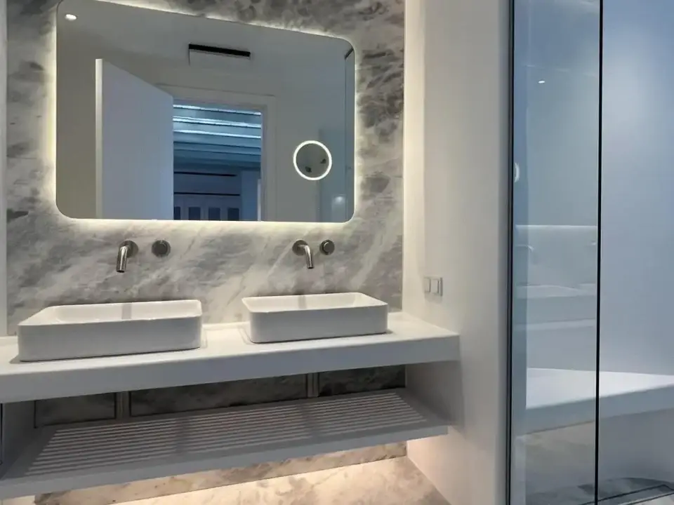 The Cave Pool Experience Suite: Modern bathroom with double sinks, backlit mirror, and marble finishes