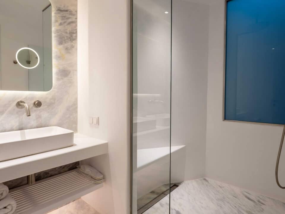 The Cave Pool Experience Suite: Modern bathroom with marble finishes, a glass shower, and a backlit vanity mirror