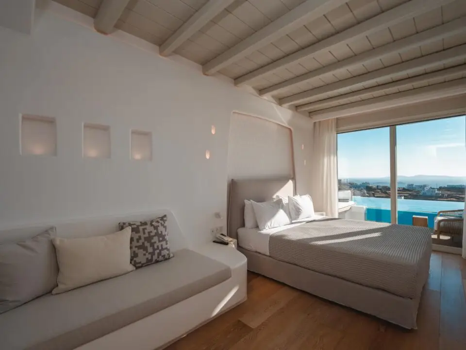 Premium Suite with Private Heated Swimming Pool: Modern bedroom with a king-sized bed, sofa, and a sliding door opening to a sea view and private pool