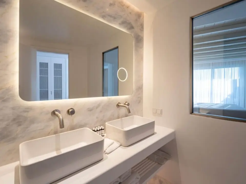 Premium Suite with Private Heated Swimming Pool: Modern bathroom with double vessel sinks, backlit mirror, and a window into the bedroom