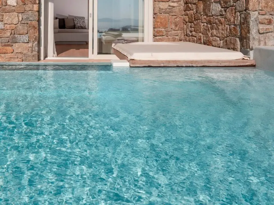 Premium Suite with Private Heated Swimming Pool: Luxury poolside patio with stone walls, sliding glass doors, and a cushioned daybed
