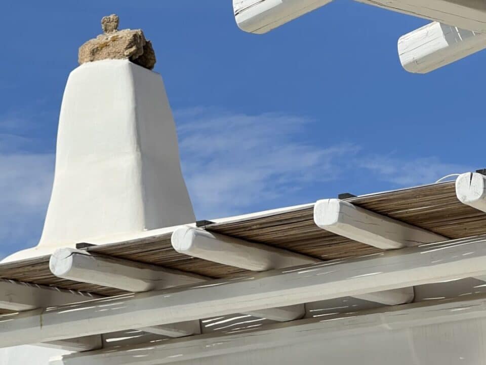 Nomia Mykonos Sunset Suites Architecture: White stucco building with wooden beams and a blue sky overhead