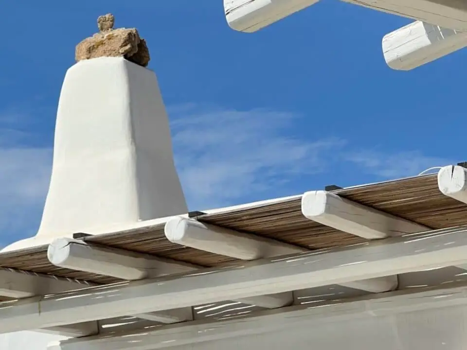 Nomia Mykonos Sunset Suites Architecture: White stucco building with wooden beams and a blue sky overhead