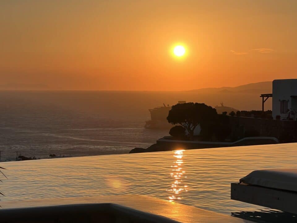Nomia Mykonos Sunset Suites: Sunset over the sea with the sun reflecting on infinity pool, viewed beside a white building