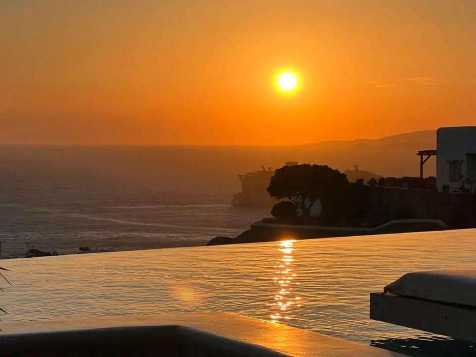 Nomia Mykonos Sunset Suites: Sunset over the sea with the sun reflecting on infinity pool, viewed beside a white building
