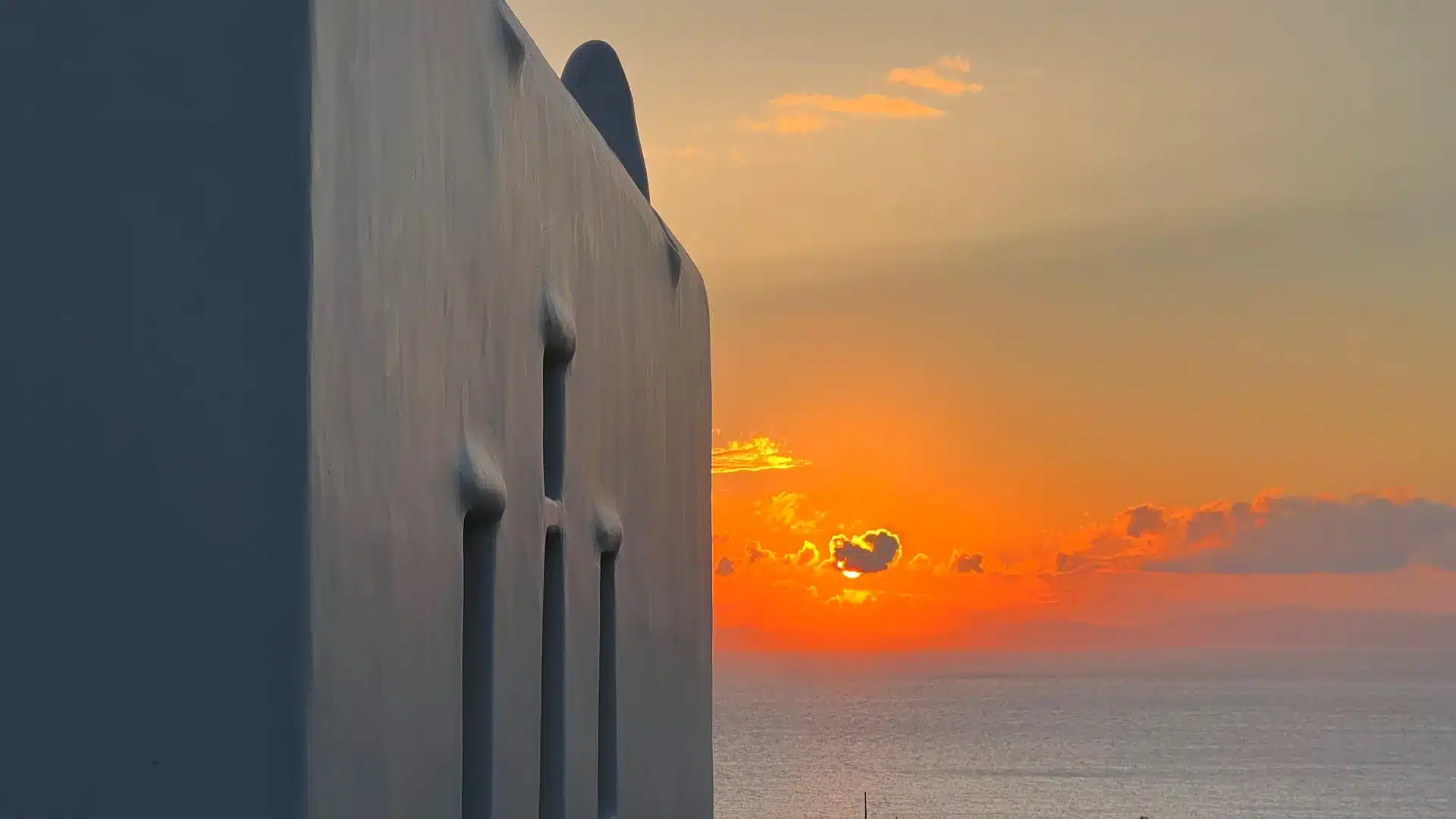 Nomia Mykonos Sunset Suites: Sunset over the ocean beside a white building wall with narrow windows