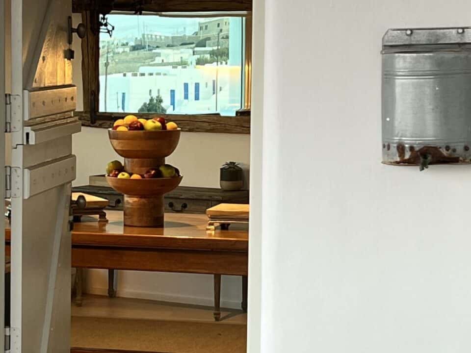 Nomia Mykonos Sunset Suites Architecturre: Authentic entrance room with a wooden table, fruit bowl, and view into a rustic kitchen through an open doorway