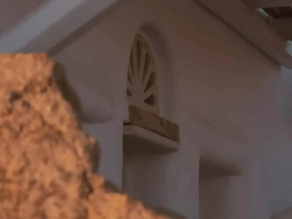 Nomia Mykonos Sunset Suites Architecture: Close-up of a traditional Mykonian white building facade with a small arched window, partly obscured by a rock in the foreground
