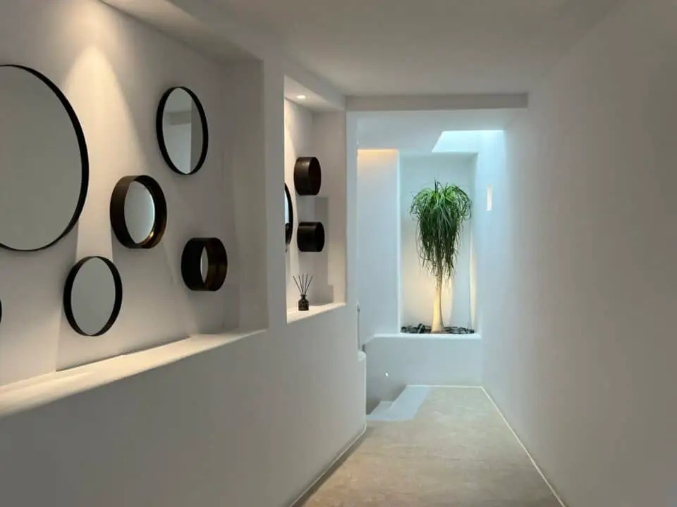 Nomia Mykonos Sunset Suites Interior: Modern white hallway with circular wall mirrors and a potted tree in a lit alcove