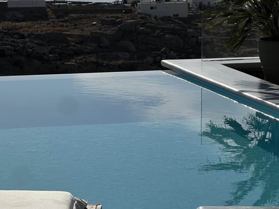 Nomia Mykonos Sunset Suites Infinity pool overlooking the sea with boats and distant mountains in the background
