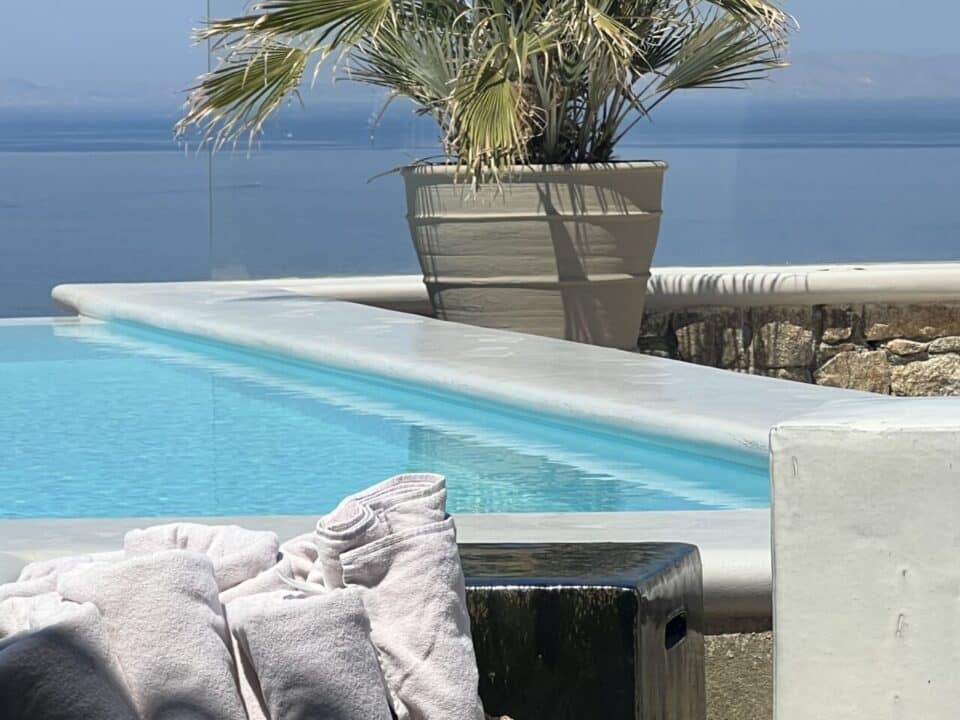 Nomia Mykonos Sunset Suites Poolside lounge with towels, a potted palm, and an Aegean view