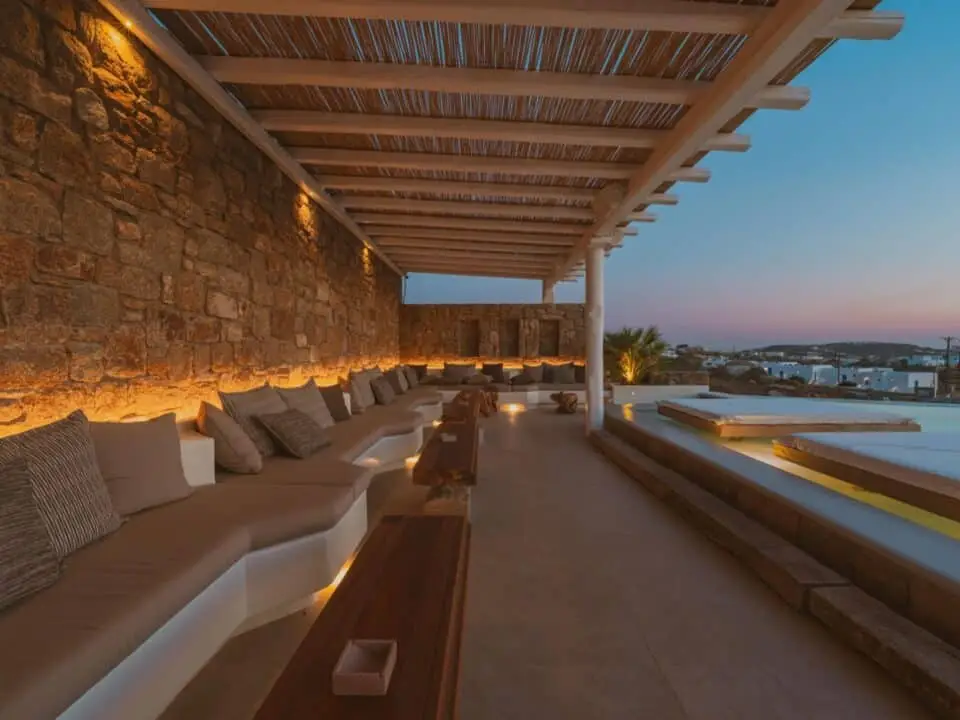Nomia Mykonos Sunset Suites Lounge Area: Outdoor lounge with stone wall seating and a poolside view at sunset