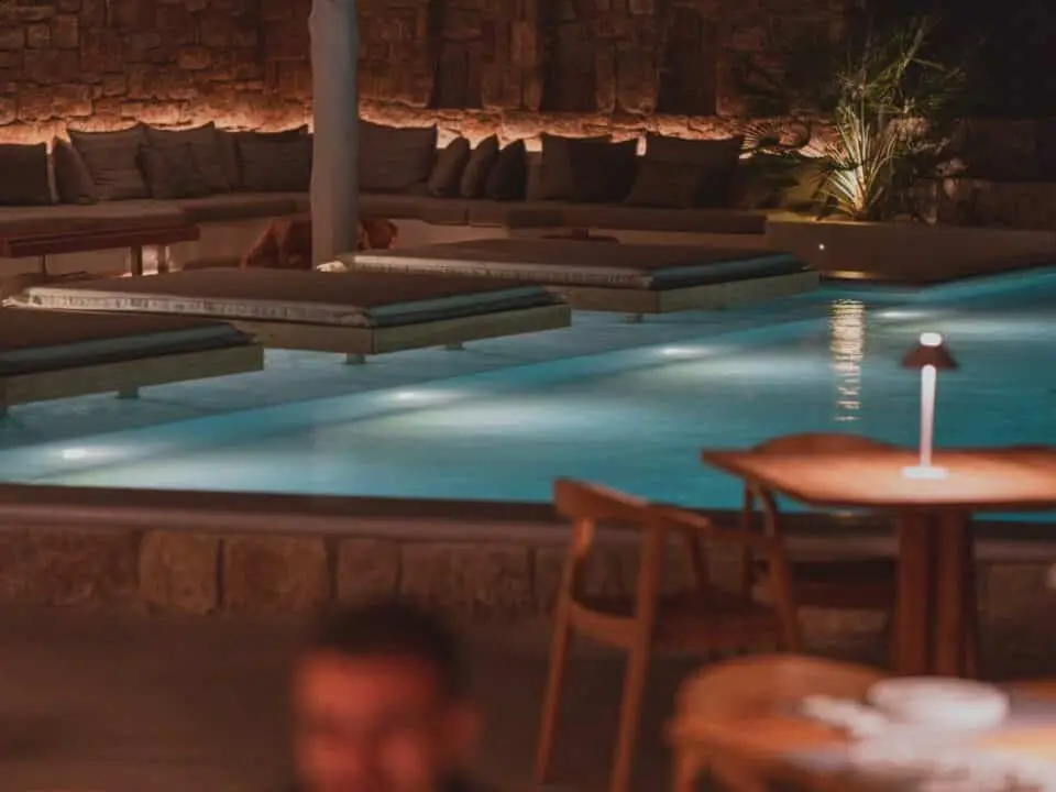 Nomia Mykonos Sunset Suites Lounge Area: Nighttime poolside lounge with cushioned daybeds, stone walls, and soft lighting